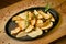 Fried potatoes in a cast-iron pan with rosemary and pepper. On a wooden stand