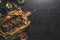 Fried ribs with BBQ sauce and various pickled vegetables on black concrete kitchen table with rosemary, wooden cutting board and