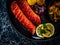 Fried sausages, fried potatoes, onion and fresh vegetables on black table