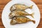 Fried short-bodied mackerel on white plate with wooden background.