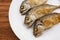 Fried short-bodied mackerel on white plate with wooden background.