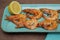 Fried shrimps with lemon on a blue plate on a wooden background and fabric napkin. Banner, menu, poster. Copy space.