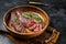 Fried sirloin flap or flank beef steak with herbs in a wooden plate. Black background. Top view