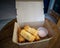 Fried spring rolls in a brown takeaway container with creamy sauce