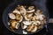 Fried steaming mushrooms in a pan on a black glass-ceramic cooktop, healthy vegetarian cooking concept