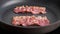 Fried strips of bacon on black frying pan. Breakfast concept.