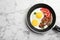 Fried sunny side up eggs with tomato and bacon in pan on marble background, top view