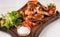 Fried tiger shrimps with lemon, vegetables, sauce and greens on a wooden cutting board