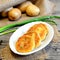 Fried vegetable patties. Potato patties with vegetables and spices on plate. Raw potatoes, fresh green onions on wooden table