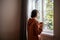 Friendless teen girl standing near window, dreaming of walking in street in warm sunny weather