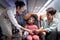 Friendly air hostess take care kid passenger on airplane, flight attendant teach curly hair African girl to use seat belt during