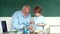 Friendly child boy with old mature teacher in classroom near blackboard desk. Grandfather and grandson. Grandfather and