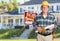 Friendly Contractor With Plans and Hard Hat In Front of Sold For Sale Sign