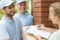 Friendly couriers in blue uniforms and woman signing receipt of package delivery