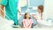 Friendly dentist talks with young patient while assistant examines her