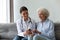 Friendly doctor consulting older woman patient, holding bottle with medicine