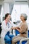 Friendly Female Head Nurse Making Rounds does Checkup on Patient Resting in Bed. She Checks tablet while Man Fully Recovering