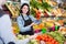 friendly female seller assisting customer to buy fruit and vegetables in grocery shop