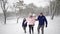 Friendly full family walking through winter forest on vacation under snowfall. Father, mother, son and daughter rest on