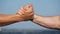 Friendly handshake of two unrecognizable muscular white men on blue sky background. Shaking of male arms outdoor. Two