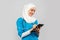 Friendly, Muslim doctor or nurse woman in a hijab with a stethoscope writes a prescription on pills on a gray background