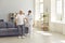 Friendly nurse helps an elderly patient walk around the room in a nursing home holding his hand.