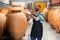 Friendly owner in protective mask of winery standing with wine in wooden barrels cellar