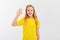 Friendly teen girl says hello, waves hand and smiles happy at you, stands in empty yellow tshirt over white background