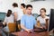 Friendly teen schoolgirl helping interested focused male classmate sitting at computer in information technology class