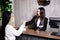 Friendly young concierge standing behind a reception counter giving room information to guest checking into a hotel