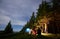 Friends around the campfire in evening near campsite against backdrop of mighty pine forest