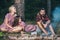 Friends camping in forest. Playful girls and boy with serious look sitting by campfire and flying sausages.