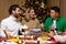 Friends celebrate Christmas eve or New Year holiday paty together sitting at the table. Feast at home group of multi