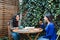 Friends and Coffee: Cafe Patio with lush foliage Hosts Two Young Latina Women Enjoying Coffee and Sweet Pastries