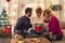 Friends enjoying moment of sharing and opening presents by Christmas tree in living room