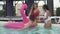 Friends having fun in the swimming pool. Two beautiful slender playful girls in swimsuits turn the guy sitting on an