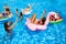 Friends having party in private holiday villa swimming pool. Happy young people swim on inflatable flamingo, swan at