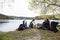 Friends Looking At Man Preparing Bonfire On Lakeside Camping