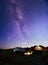 Friends near Bonfire, Pickup Truck, Tent and Bike in the Mountains under Night Sky with Milky Way. Adventure and Travel