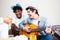 Friends playing guitar and singing together in living room with food snacks and drinks. Playful youth, enjoyment