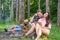 Friends relaxing near campfire after day hiking or gathering mushrooms. Summer vacation forest. Company friends couples