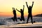 Friends silhouette jumping happy on the beach at sunset