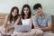 Friends sit together in bed, while the beautiful girl in the middle holds a laptop in hand