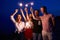 Friends walking, dancing and having fun during night party at the seaside with bengal sparkler lights in their hands