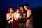 Friends walking, dancing and having fun during night party at the seaside with bengal sparkler lights in their hands