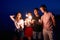 Friends walking, dancing and having fun during night party at the seaside with bengal sparkler lights in their hands