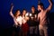 Friends walking, dancing and having fun during night party at the seaside with bengal sparkler lights in their hands