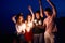 Friends walking, dancing and having fun during night party at the seaside with bengal sparkler lights in their hands