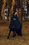 Friesian horse stays on one knee while training with a young woman in a black evening Gothic attire riding horseback