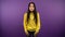 A frightened Asian woman in a yellow sweater jumps back. woman on purple isolated background. 4K